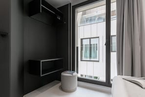 Una camera moderna con una grande finestra, un pouf bianco e scaffali a muro.
