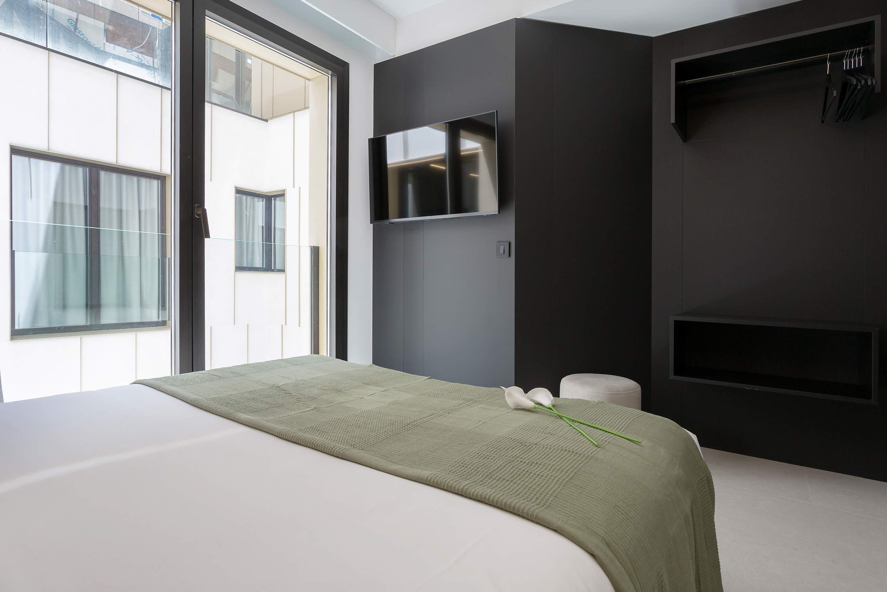 Un dormitorio moderno con una cama grande, un televisor de pantalla plana en la pared y una ventana con cortinas.