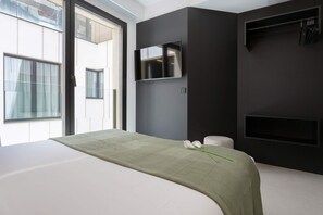 A modern bedroom with a large bed, a flat-screen TV mounted on the wall, and a window with curtains.