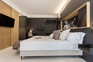 A modern bedroom with a large bed, a mounted TV, and a painting on the wall.