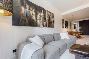 A modern living room with a grey sofa, a large abstract painting, and a dining area with a table and chairs. - Spectacular Apartment in Valladolid Center Solanilla III (Valladolid)