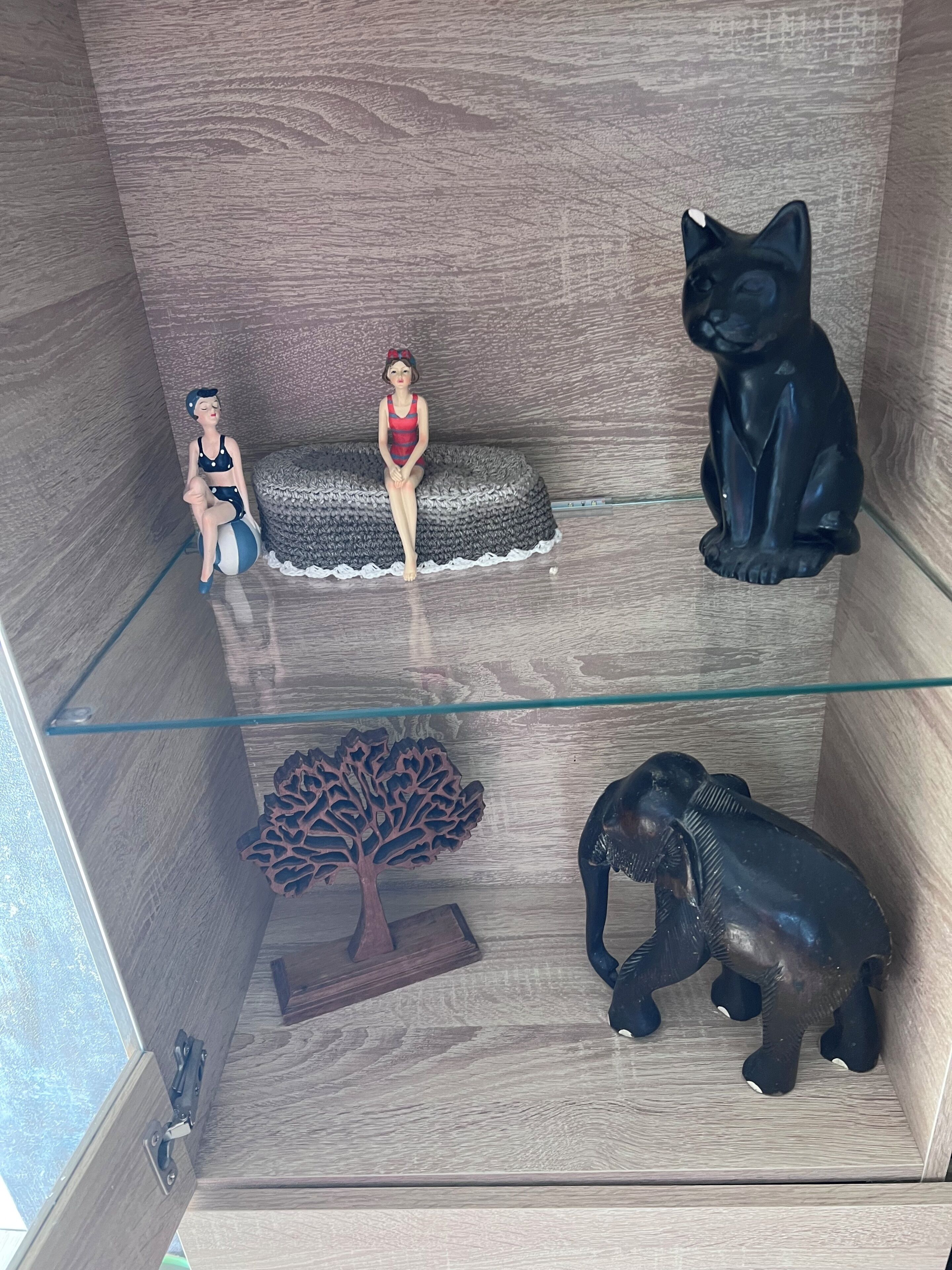 A room with a glass partition, a small sofa, a decorative tree, and a figurine of an elephant.