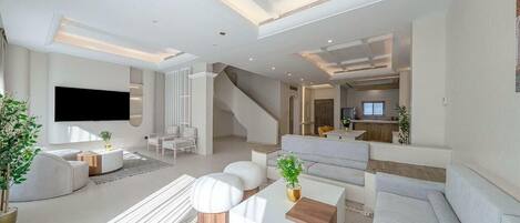 A modern living room with a flat-screen TV, sofas, a coffee table, and a staircase leading to an upper level.