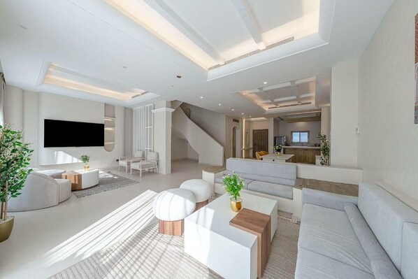 A modern living room with a flat-screen TV, white sofas, a coffee table, and a staircase leading to another level.