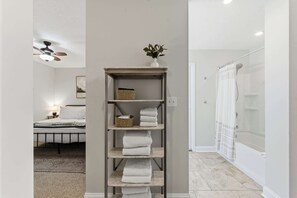 A bathroom with a shower, a glass-enclosed toilet, and a towel rack with folded towels. - The Cottage Nook l Hot Tub l Mins to DNTN (St. Augustine)