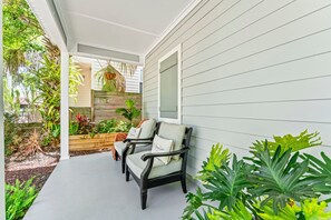 Eine überdachte Veranda mit zwei Stühlen, einem Holzpflanzgefäß und verschiedenen Pflanzen.