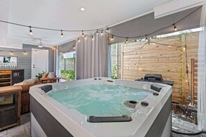 Een hottub met een houten terras, een tafel met stoelen en lichtslingers.