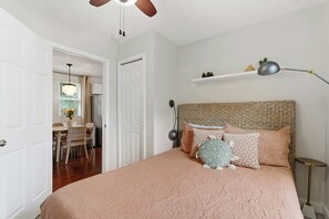 Ein Schlafzimmer mit Bett, Kopfstütze, Nachttisch, Lampe und einer Tür zu einem Essbereich.