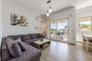 A modern living room with a sectional sofa, a coffee table, and a dining area with a table and chairs. - Beachside Family Apartment Balcony Parking (Ishëm)