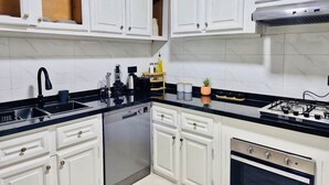 Una cocina con armarios blancos, encimera negra, lavavajillas, estufa y fregadero.
