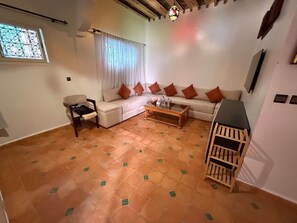 Ein Wohnzimmer mit einer Couch, einem Couchtisch, einem Sessel, einem Fernseher und einem kleinen Holzregal.