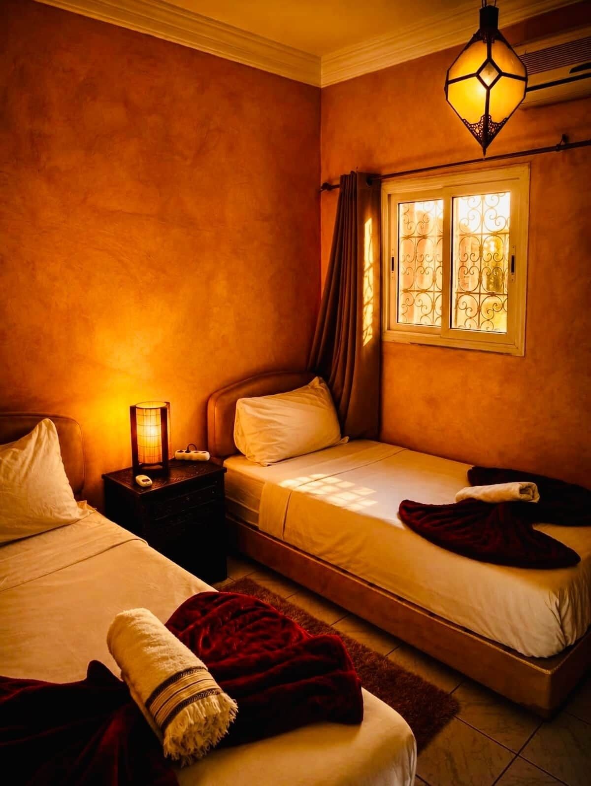 A bedroom with two beds, a nightstand, a lamp, and a window with curtains.