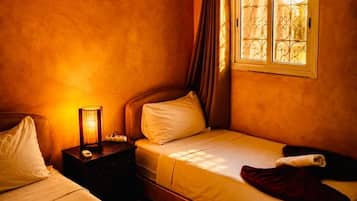 A bedroom with two beds, a nightstand, a lamp, and a window with curtains.
