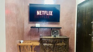 Ett rum med en tv monterad på väggen som visar "NETFLIX", ett träbord med en stol och ett dekorativt skåp.