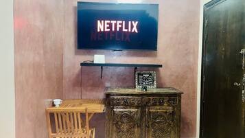 A room with a television mounted on the wall displaying 'NETFLIX,' a wooden table with a chair, and a decorative cabinet.