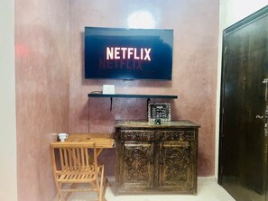 Ein Zimmer mit an der Wand befestigtem Fernseher, der 'NETFLIX' zeigt, einem Holztisch mit Stuhl und einem dekorativen Schrank.