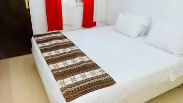 A bed with white bedding and a patterned blanket, red curtains, and a door with a yellow handle.