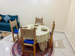 A round dining table with a lace tablecloth, surrounded by woven chairs with blue cushions, set on a patterned rug. - Family-friendly home in the city center, a 5-minute walk from the train station (Marrakesh)