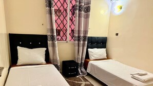 Camera d'albergo con due letti, una finestra con tende rosa, una testata nera e un comodino nero.