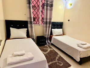 A hotel room with two beds, a window with pink curtains, a black headboard, and a small black side table. - Family-friendly home in the city center, a 5-minute walk from the train station (Marrakesh)