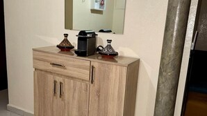 Un mobiletto in legno con cassetti e uno specchio sopra, una colonna in metallo e un pavimento piastrellato.
