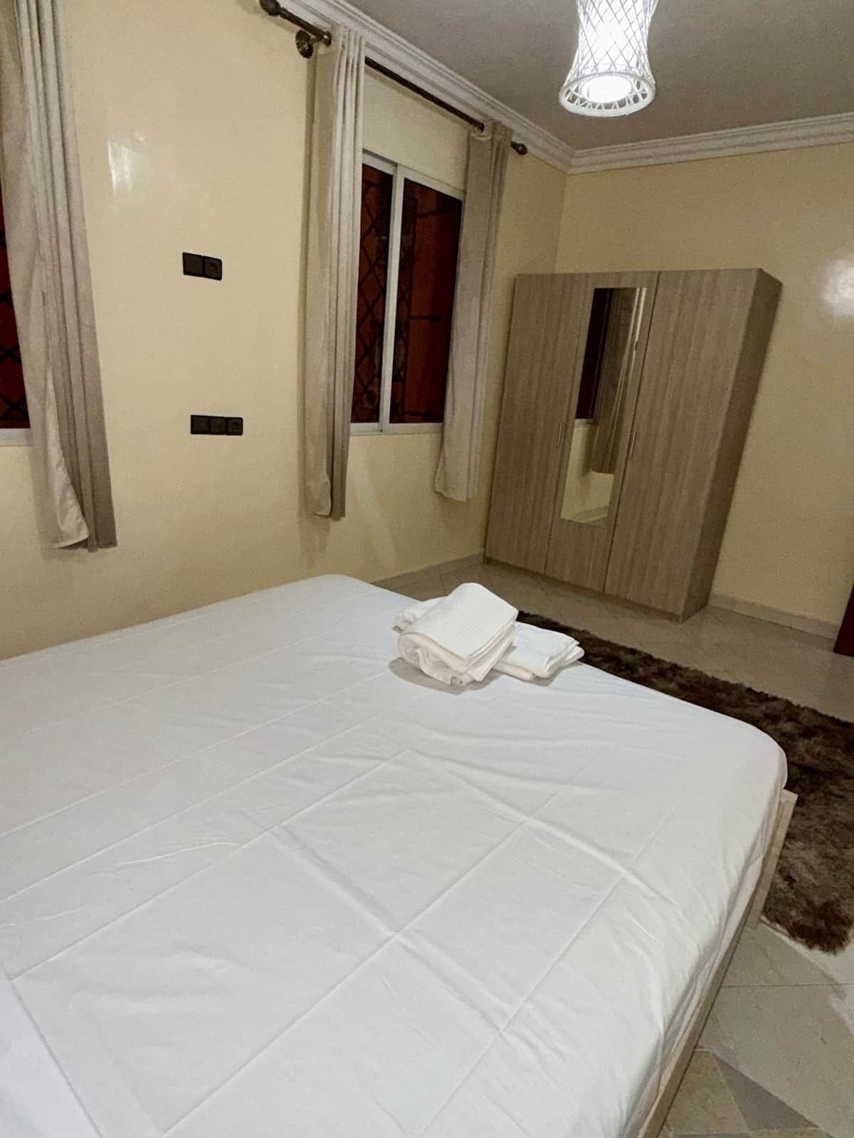 Ein Schlafzimmer mit Bett, Kleiderschrank, einem Fenster mit Vorhängen und einem Spiegel.
