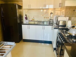A kitchen with a black refrigerator, white cabinets, a stove, and a sink. - A Luxurious, Modern, Central Gem + Netflix (Marrakesh)