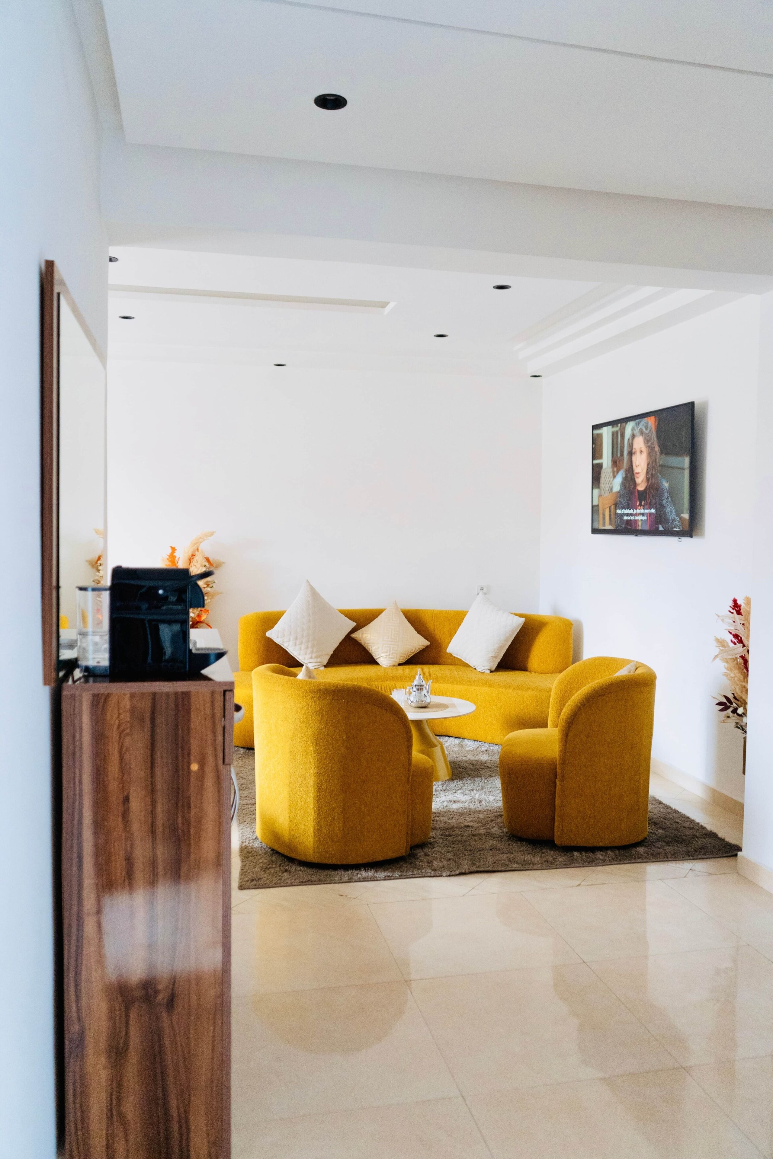 A modern living room with a yellow sofa, a coffee table, and a flat-screen TV mounted on the wall.