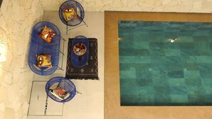 Area piscina con pavimento piastrellato, una piscina e tre sedie blu con cuscini.