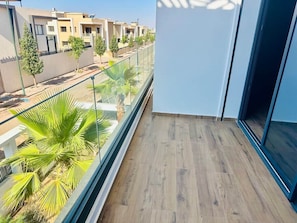 Ein Balkon mit Holzboden, Glasgeländer und Blick auf benachbarte Gebäude und Bäume.