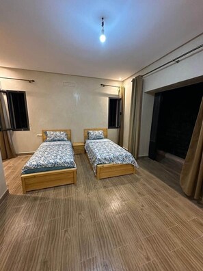 A room with two wooden beds, a ceiling light, and a window with curtains.