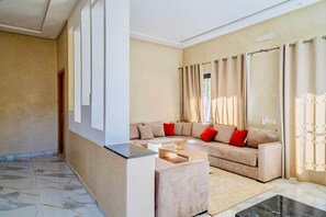 A living room with a beige sofa, red cushions, a coffee table, and a patterned rug.