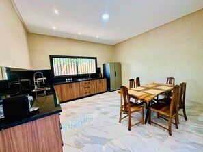 A modern kitchen with a dining area, featuring a marble floor, wooden cabinets, and a large window.