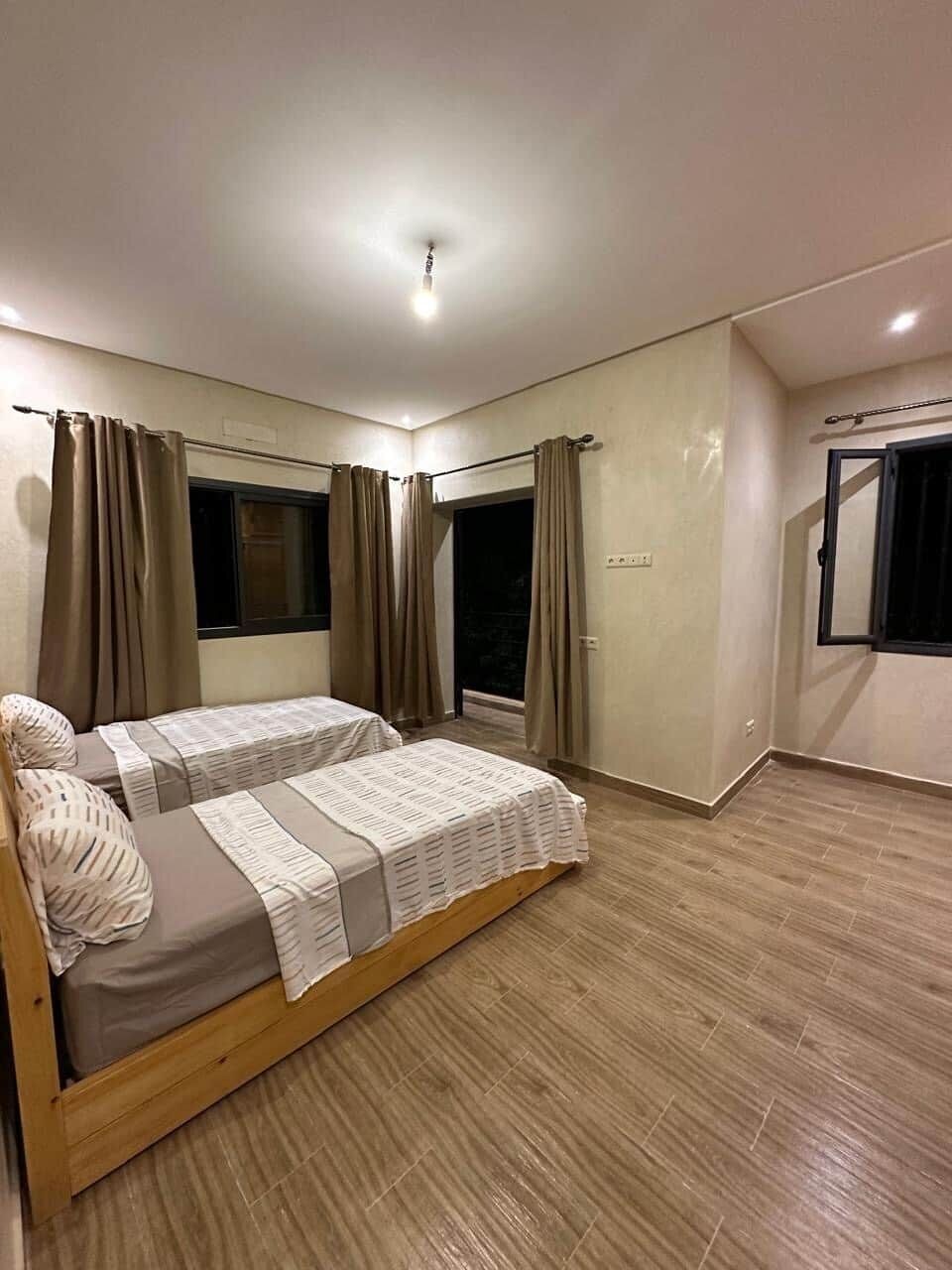 A bedroom with two beds, a window, a door, and a light fixture.