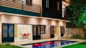 Une maison moderne à deux étages, dotée d’une piscine, de grandes portes-fenêtres coulissantes et d’un balcon.