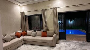 Un salon moderne avec un canapé d’angle, une piscine et une grande fenêtre.