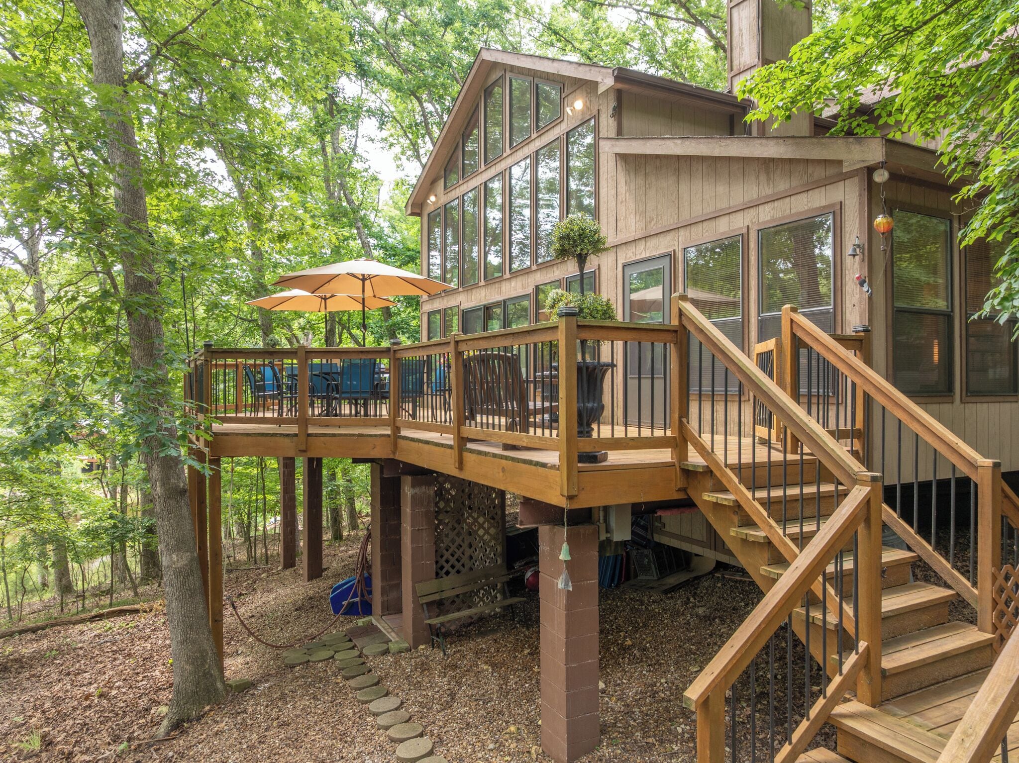 A wooden deck with outdoor furniture and umbrellas, a staircase, and a building with large windows.
