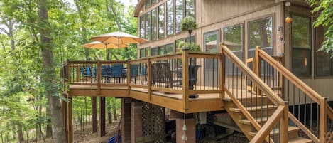 Una terraza de madera con mobiliario exterior y sombrillas, una escalera y un edificio con grandes ventanales.