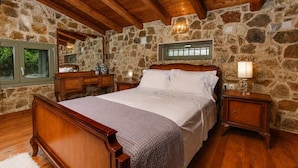 Une chambre avec un mur en pierre, des poutres en bois au plafond, un lit, une table de chevet et une fenêtre.