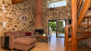 Une pièce aux murs de pierre, avec un canapé, une cheminée et un escalier en bois.