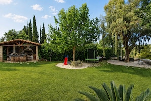Un jardin avec un espace barbecue, une balançoire et une table à manger entourée de chaises.
