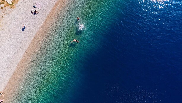 Une plage à l’eau claire, où l’on peut voir des gens se baigner, et une structure en bois sur le sable.