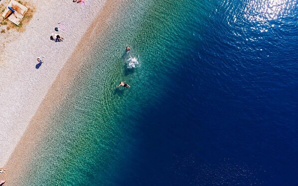 A beach with clear water, people swimming, and a wooden structure on the sand.
