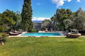 A swimming pool with lounge chairs, a stone fire pit, and a view of the mountains. - Blue Jasmine Villa - Private Pool and Garden (Aigialeia)