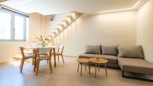 A modern living room with a sofa, dining table, chairs, and a staircase. - Neilise - Modern Retreat in Central Kalamata (Kalamata)