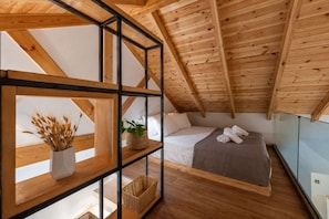 A high-ceilinged room with wooden beams, a bed with white linens, a small table with a plant, and a window overlooking a balcony. - Neilise - Modern Retreat in Central Kalamata (Kalamata)