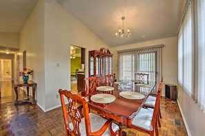 A dining room with a wooden table and chairs, a chandelier, and a view of a hallway.