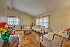A living room with a sofa, armchairs, a coffee table, and a vase of flowers.