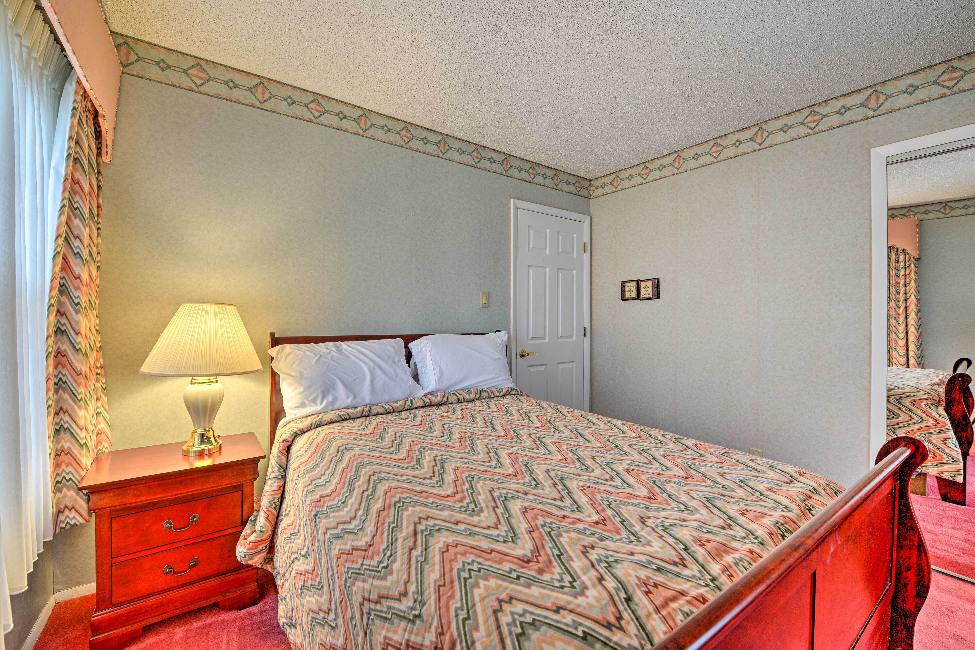 A bedroom with a bed, a nightstand, a lamp, a door, and a mirror.