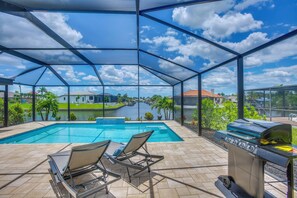 Ein überdachter Außenbereich mit Pool, Liegestühlen und Grill.